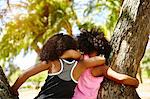Two young sisters playing on tree. rear view