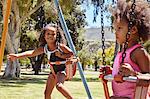 Two young sisters playing on park swings