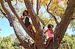 Two young sisters climbing tree