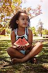 Portrait of young girl, sitting on grass, eating watermelon