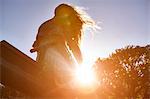 Girl sitting on see-saw, bright sunlight shining through trees, low angle view