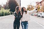 Twin sisters, walking outdoors, taking selfie using smartphone