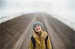 Portrait of girl in knit hat standing in middle of foggy dirt road laughing