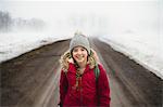 Portrait of girl in knit hat standing in middle of dirt road in fog