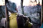 Rear view of mature woman sitting on woodland porch watching sunset