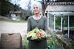 Portrait of mature female gardener with bowl of tomatoes and spring greens