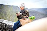 Woman sitting on wall texting on smartphone, Bruniquel, France