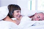 Couple laughing under duvet on bed