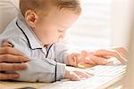 Mother typing with baby looking interested in keyboard