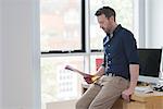 Man contemplating and reading papers by office window