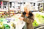 Mature woman in supermarket, putting fresh produce in plastic bag