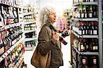 Mature woman in supermarket, holding bottles of alcohol