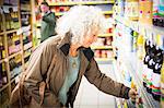 Mature woman in supermarket, taking bottle of juice from shelf