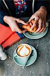 Overhead view of woman's hand holding croissant in cafe
