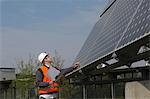 Young male engineer using digital tablet looking up at solar panels