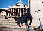 Businessman beside scooter, Trafalgar Square, London, UK