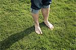 Legs and bare feet of man standing on green grass