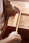 Hands of male carpenter measuring frame at workbench