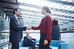 Businessman and woman shaking hands in office atrium