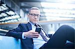 Businessman on sofa looking at smartphone in office atrium