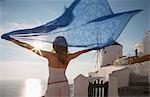 Woman arms raised holding kaftan looking away at view of sea, Santorini, Cyclades, Greece