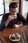 Young couple sitting at table, drinking coffee, pastries on table, focus on man
