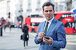 Businessmen in street with smartphone and earbuds, London, UK