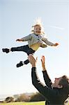 Female toddler thrown mid air by father against blue sky