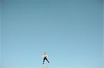 Distant view of female toddler thrown mid air against vast blue sky