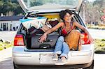 Woman sitting in car boot with luggage laughing