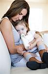 Female toddler on mother's lap drinking from baby bottle