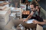 Man with clipboard checking boxed products in factory