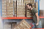 Man pushing sack trolley of stacked cardboard boxes in factory