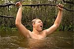 Teenage boy in water holding tree branch jubilantly, Turkey Creek, Niceville, Florida, USA