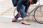 Young male cyclist rolling down jeans on railway station platform