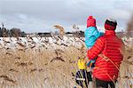 Father and two sons walking through long grass, in snow covered landscape, rear view