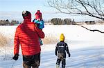 Father and two sons walking in snow covered landscape, rear view