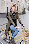 Portrait smiling young woman with headphones riding bicycle with produce in basket