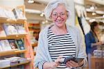 Portrait smiling mature female shopper using cell phone in shop