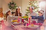 Family in paper crowns pulling Christmas cracker at dining table