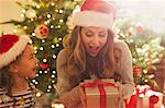 Surprised mother with Santa hat receiving Christmas gift from daughter