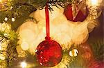 Close up red sequin ornament hanging from branch of Christmas tree with string lights