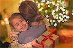 Smiling daughter with Christmas gift hugging mother