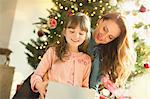 Mother watching daughter opening Christmas gift