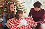 Parents giving large Christmas gift to daughter in front of Christmas tree