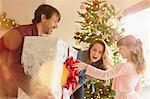 Parents giving large Christmas gift to daughter near Christmas tree