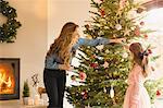 Mother and daughter hanging ornaments on Christmas tree