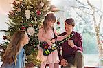 Parents watching daughter playing toy guitar Christmas gift in front of Christmas tree