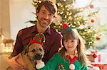 Portrait smiling father, daughter and dog in front of Christmas tree