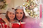 Portrait enthusiastic mother and daughter in paper crowns at Christmas dinner table